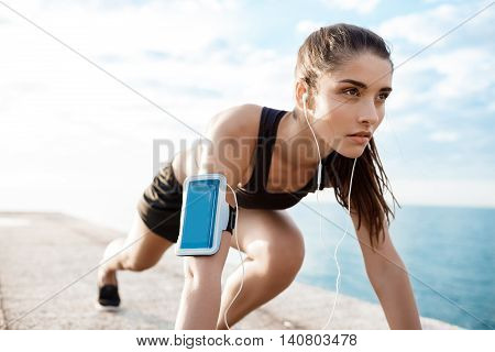 Young beautiful brunette sportive girl preparing to run over seaside. Copy space.
