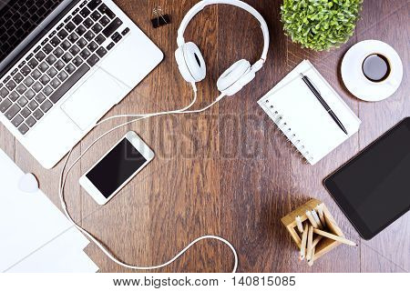 Top view of wooden desktop with tablet laptop smartphone headphones decorative plant and supplies. Mock up