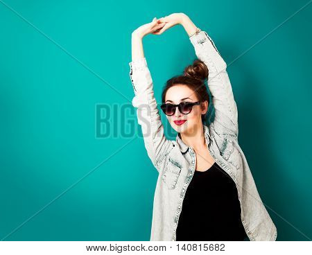 Happy Hipster Girl in Sunglasses and Jeans Shirt Posing at Turquoise Background. Street Style Fashion Outfit. Toned Photo with Copy Space.