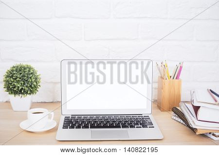 Closeup of creative hipster desktop with blank white laptop coffee cup and other stationery and decorative items on brick background. Mock up