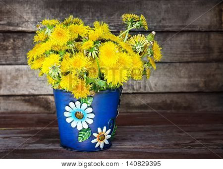 blue bucket dandelions on a wooden background