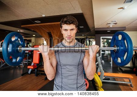 Portrait of attracitve young sportsman training using barbell in gym