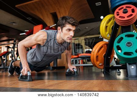 Confident young fitness man working out and doing push-ups in gym