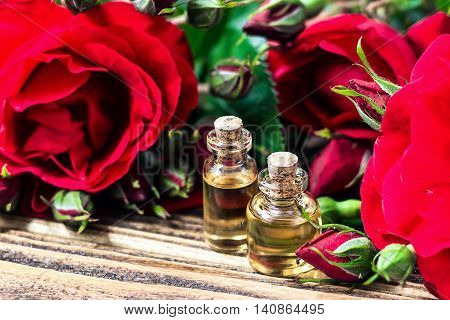Essential oil in glass bottle with red rose flowers and petals on wooden background. Beauty treatment. Spa and aromatherapy concept. Selective focus.