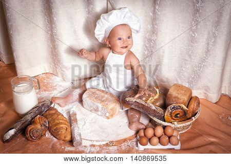 Happy baby baker sitting surrounded by bread and pastries