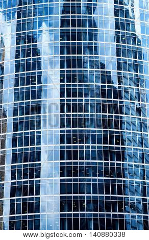 A background with the reflections of sky, clouds and buildings in the windows of a skyscraper.