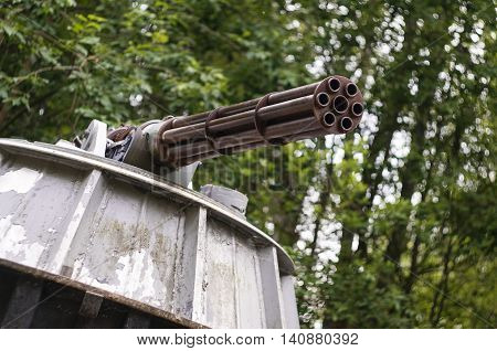 An old minigun on a stand in a forest.
