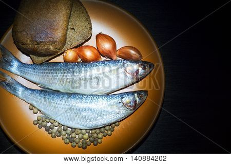 Two fish Golden grey mullet with onion allspice and rye bread on the plate on black background.