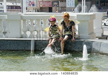Kharkiv Ukraine - June 18 2016: Mother and daughter dreessed in costumes of bees are drying their feet after washing them in the fountain. Costumed bike ride 