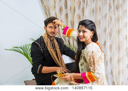 indian sister applying tika on brother's forehead, enjoying and celebrating Raksha Bandhan festival
