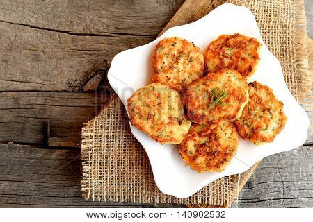 Fried salmon cutlets on a plate and on an old wooden background with free place for text. Roasted red fish patties with dill and onion. Top view