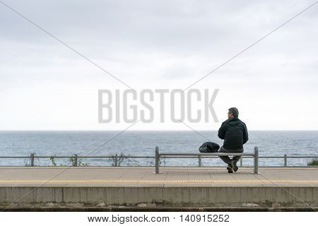 Corniglia Italy - Apr 8 2016: Unidentified backpacker old man tourist wait for train by the ocean with gloomy sky background looking at copy space at Corniglia train station Cinque Terre Italy