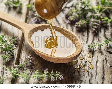 Herbal honey pouring into the wooden spoon. Spoon is on old wooden table surrounded with levender flowers.