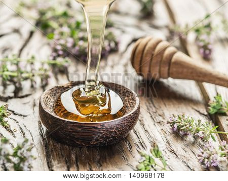 Herbal honey pouring into the wooden bowl. Bowl is on old wooden table surrounded with levender flowers.
