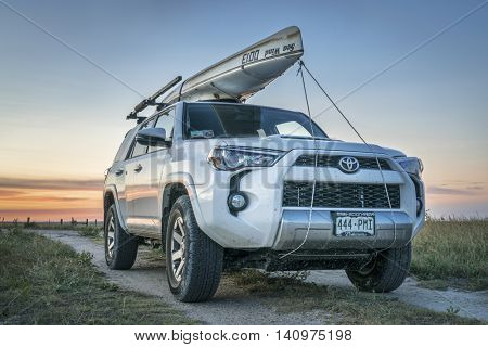CASTLE ROCK, KS , USA - JULY 25 2016: Toyota 4Runner SUV (2016 Trail edition) with a canoe (Sea Wind by Kruger Canoes) on roof racks driving during summer vacations on Kansas  back country roads