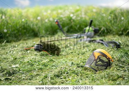 String Trimmer And Protective Face Mask On Mown Grass, Growing Grass And The Blue Sky On The Backgro