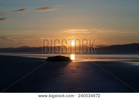 A Stunning Sunset On Benone Beach, With A Sillhouette Of A Rock In The Foreground.