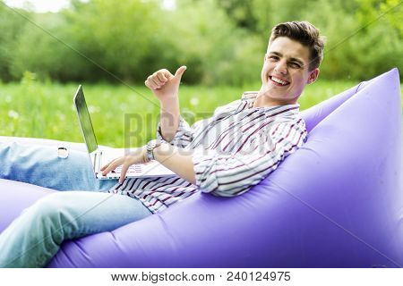Handsome Young Smile Man Lying On Inflatable Sofa Lamzac Working On Laptop And Gesturing Thumbs Up W