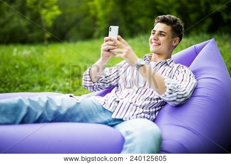 Handsome Young Smile Man Lying On Inflatable Sofa Lamzac Browse In App On Phone While Resting On Gra
