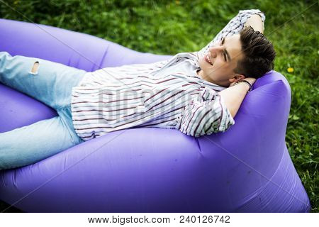 Feel Free. Handsome Young Man Lying On Inflatable Sofa Lamzac While Resting On Grass In Park