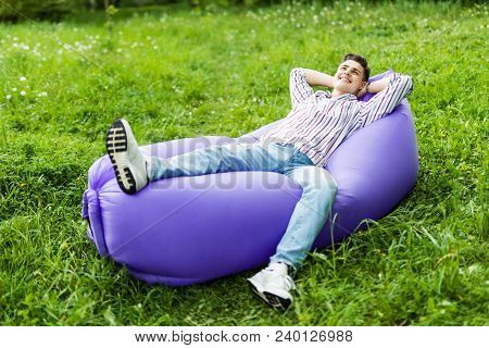 Handsome Young Man Lying On Inflatable Sofa Lamzac While Resting On Grass In Park On The Sun