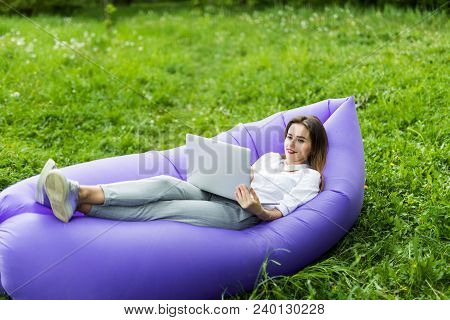 Pretty Young Woman Lying On Inflatable Sofa Lamzac Use Laptop While Resting On Grass In Park