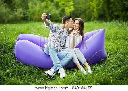 I Love You Too Much. Young Couple Kissing Sitting On Inflatable Sofa Lamzac And Take Selfie On Phone