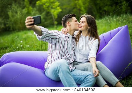 I Love You Too Much. Young Couple Kissing Sitting On Inflatable Sofa Lamzac And Take Selfie On Phone