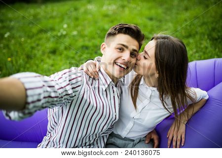 Young In Love Couple Kissing While Sitting On Inflatable Sofa Lamzac And Take Selfie On Phone Restin