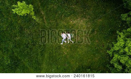 Above View Of Young Couple Holding Hands While Lying On The Grass Like Running. Summer Fun