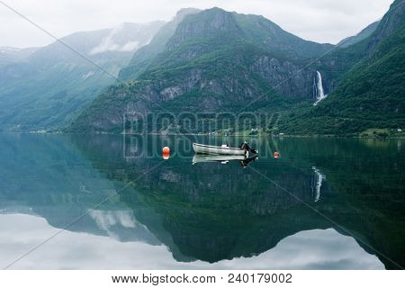 Norwegian landscape with mountain and Feigumfossen waterfall. White boat in the Lusterfjord fjord. Summer day. Commune Luster, Norway