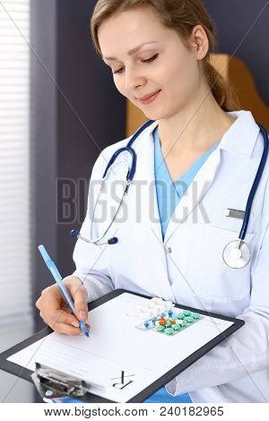 Woman Doctor Write Prescription While Sitting In Hospital Office. A Lot Of Various Colored Pills Liy
