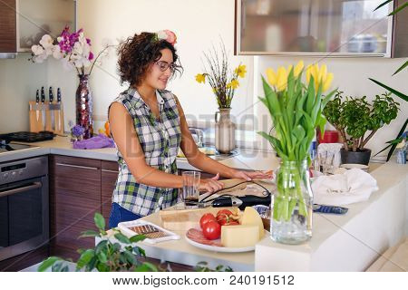 Positive Brunette Female With Curly Hair Makes Salad With Tomatoes And Potato In A Home Kitchen.