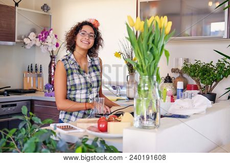 Positive Brunette Female With Curly Hair Makes Salad With Tomatoes And Potato In A Home Kitchen.