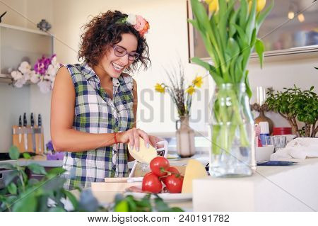 Positive Brunette Female With Curly Hair Makes Salad With Tomatoes And Potato In A Home Kitchen.