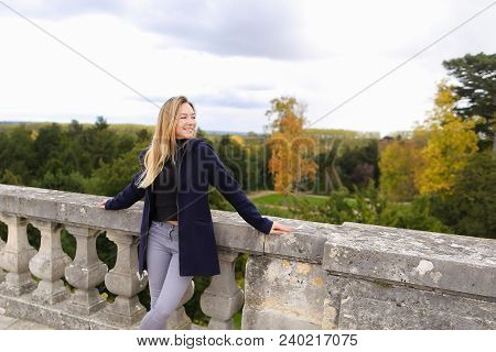 Young Woman Standing Near Concrete Railing With Green Trees Background. Concept Of Architectural Ele