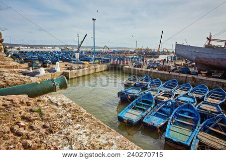 Essaouira Port In Morocco With Blue Fishing Boats And Ancient Famous Fort On Background On A Sunny D