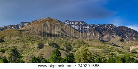 Dark Storm Forming Above The Rocky Mountains With Green Foothills In The Foreground