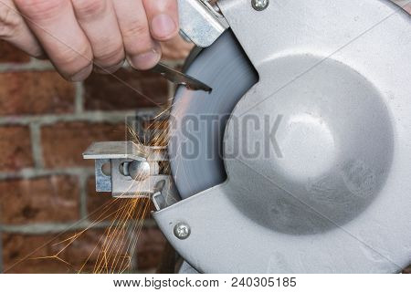 A Knife Sharpener And Hand With A Blade On A Wooden Table, Close-up Against A Brick Wall Background