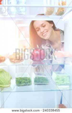 Portrait of female standing near open fridge full of healthy food, vegetables and fruits. Portrait of female