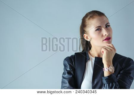 portrait of beautiful young brunette woman in stylish black jacket on gray.