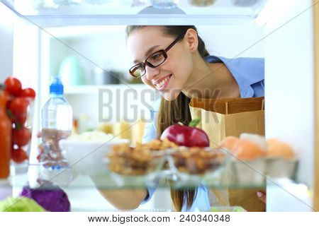 Portrait of female standing near open fridge full of healthy food, vegetables and fruits. Portrait of female