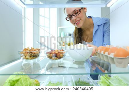 Portrait of female standing near open fridge full of healthy food, vegetables and fruits. Portrait of female