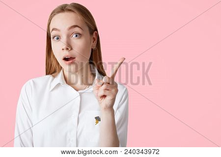 Lovely Young Female Remembers About Important Meeting, Keeps Fore Finger Raised Or Gets Idea, Wears 