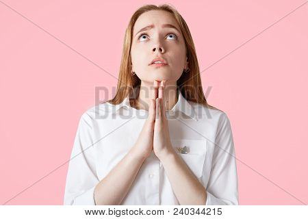 Horizontal Portrait Of Hopeful Female Keeps Palms Pressed Together, Has Big Hope, Prays In Studio Is