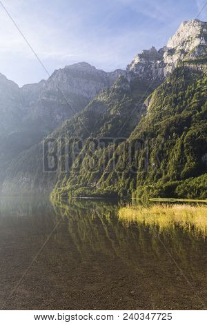 Sunny  Foggy Morning In The Swiss Alps. Mountain Lake Klontalersee In Haze On  Background Of Majesti