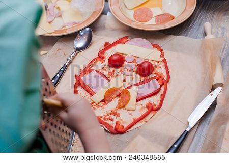 The Child Decorates The Funny Pizza - Pepper, Cheese, Sausage, Sauce Spread Out On The Dough