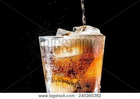 Stream Of Soda Being Pouring Into A Glass With Soda And Ice Cube On Black Background, Closeup Textur