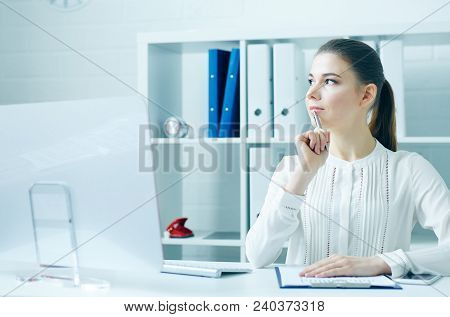 Pensive Young Business Woman Sitting At The Dask With Desktop Monitor And Looking At The Window.