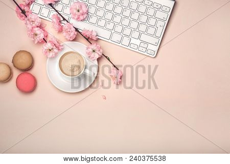 White Cup With Cappuccino, Sakura Flowers, Keyboard, Macarons On A Pastel Pink Background. Top View.